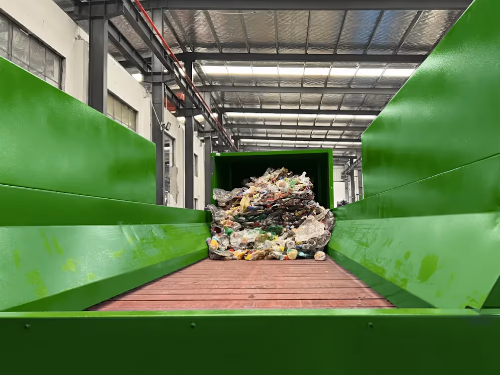 The infeed hopper of a debaler machine, showing a compressed bale of plastic bottles and containers ready to be broken apart for recycling.